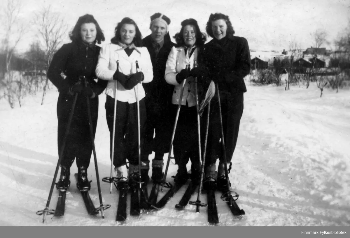 Bilde tatt på Selskapsjorda i Bjørnevatn. Fra venstre står: Solaug Nilsson g.Skare, Elsa Olsen g.Eriksen, Johan Skare, og to ukjente kvinner. De har alle på seg ski. I bakgrunnen ser man Egnehjem