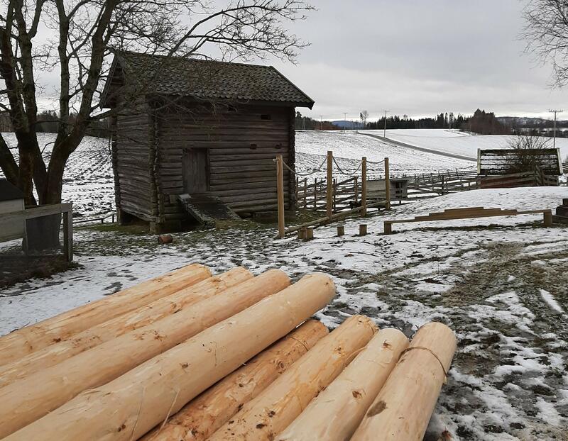 Bildet viser barkede tømmerstokker som ligger foran et laftet hus. Huset er ei gammel kvern. Det er snø på bakken.