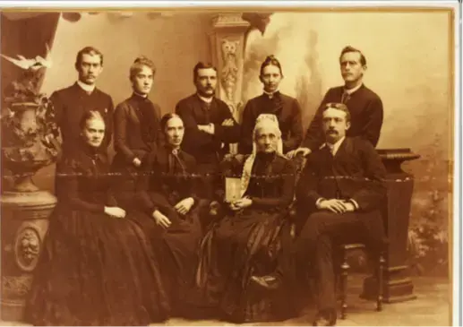 Sort-hvit bilde i bruntoner som viser et gruppebilde av ni mennesker som er oppstilt. Fem står bak. Fire sitter på stoler foran. alle er kledd i sort og har et alvorlig uttrykk.