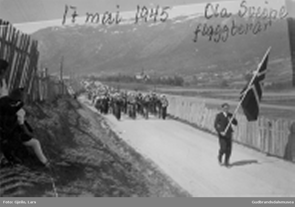Folketoget på veg frå Skjåk kyrkje 17. mai 1945. 
Ola Sveine (f. 1920) ber flagget framanfor Skjåk Musikklag