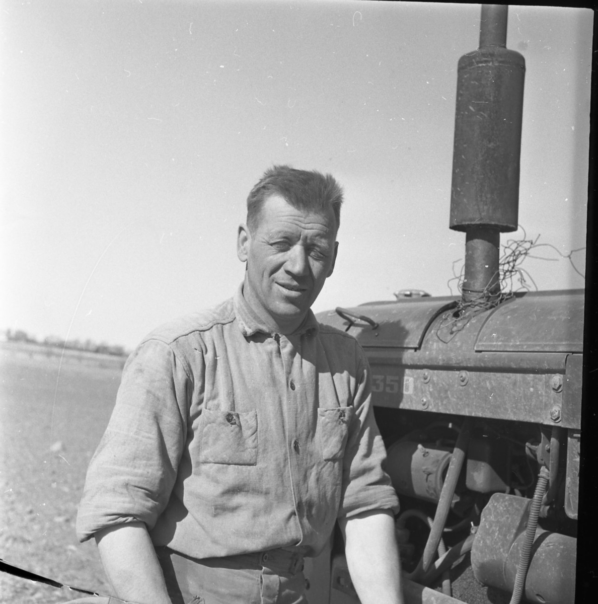 Porträtt av Per-Axel Wenner. Han bär en arbetsskjorta och står lutad mot en traktor.