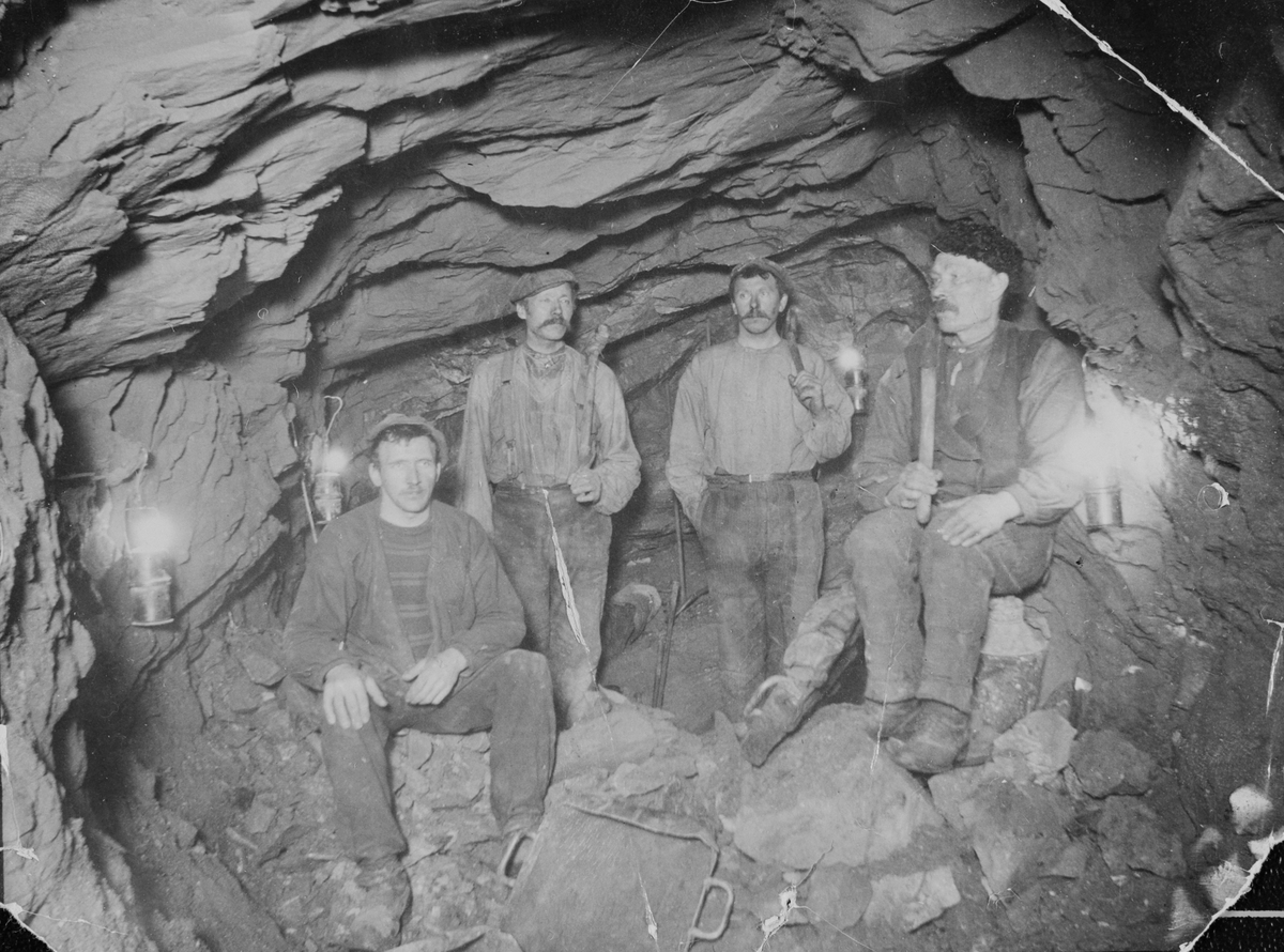 Fire gruvearbeidere med karbidlamper og redskaper i ei gruve