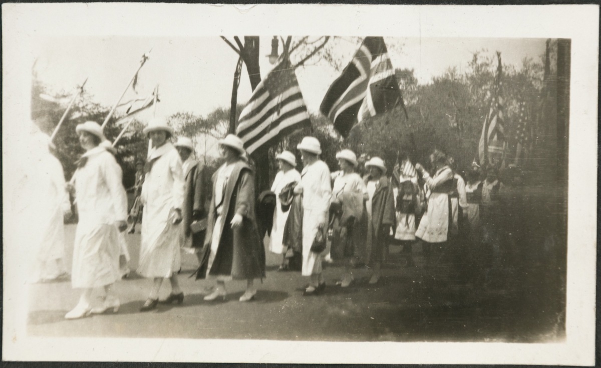 Folketog under syttende mai i USA. Kvinner i bunad og like drakter flagger med norske og amerikanske flagg.