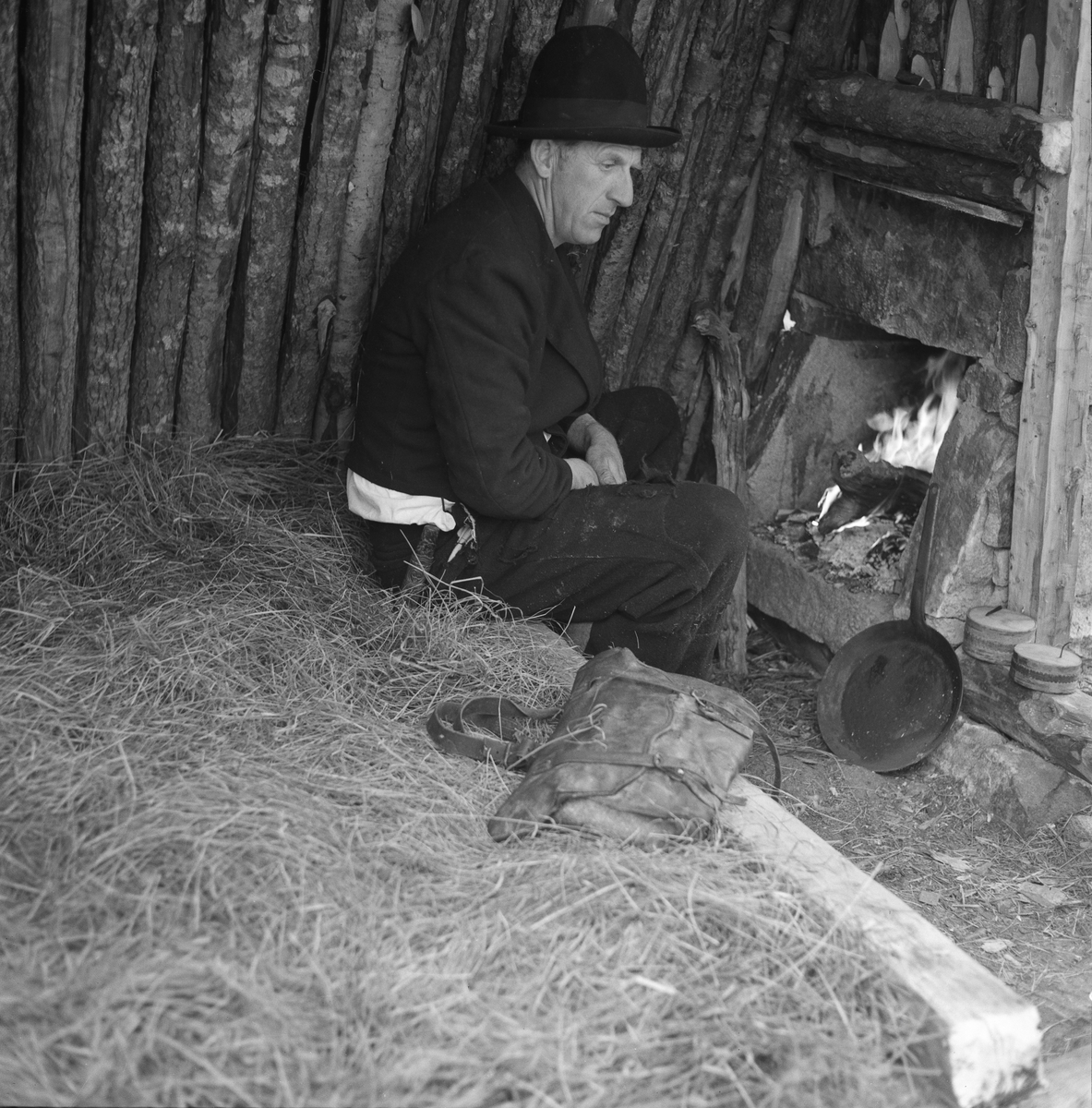 Interiør fra såkalt kjøyte (jordkoie) i Drangedal i Telemark. Kjøyta var en enkel koietype, nesten utelukkende bygd av materialer som fantes i skogen og så enkelt konstruert at skogsarbeidere uten bygningsteknisk kompetanse kunne få den ferdig på kort tid. Jørund Midttun (1887-1969), som kom til Telemark som ung forstkandidat i 1914 og ble en sentral skikkelse i skogbruket der gjennom hele sin yrkeskarriere, beskrev dette slik: 

«Framgangsmåten med oppsettinga var gjerne slik at når tre-fire hoggarar hadde teke hogst saman eller nær kvarandre, drog dei til skogs frå morgonen av, og dei rakk då å setta opp ei slik kjøyte på ettermiddagen.

Kjøyta var bygd av «props». Det var smale stokkar som vart reist opp på ei rund eller firkanta tuft nedantil. Oppe gjekk stokkane saman i topp, og kjøyta vart som eit spisstelt å sjå til. … Det var heller ikkje uvanleg at kjøyta vart sjåandes ut som ein avslutta pyramide. Slik er den Skogbruksmuseet har på Prestøya [SJF-B.0009] …

For å gjera kjøytene tette og varme, la dei granbork eller bjørkenever utanpå stokkane og deretter kom eit tjukt lag av torv eller jord. Ofte vart det på toppen og noko nedetter lagt ei hette av bork eller never. Til dør bruka dei ein lem av kløyvde bord eller skier. Denne vart passa inn i ein karm skrådd med hyttetaket og kunne berre opnast utetter. Ved sida av døra vart det på utsida av taket (veggen) mura ein peis. Sjølve grua var inne i kjøyta, men elles sjekk skorsteinen opp utanfor. Sengene (benk-brisk) gjorde dei vanlegvis også av smått rundvirke, litt opp frå bakken, slik at dei vart liggande med føtene mot døråpning og gruve.

Desse kjøytene var gode og varme, og her budde så vel bonden sjølv som folka hans på virkedagane når hogsten gjekk.»

Midttun skrev videre at «Slike kjøyter var vanlege over store luter av Telemark heilt fram til 1920-åra.» At det ble slutt med kjøytebygginga på denne tida hadde sannsynligvis samanheng med at Stortinget i 1915 vedtok en lov om husvær for folk og hester under skogsarbeid og fløting, som skulle følges opp med lokale vedtekter. Året etter fulgte herredsstyret i Drangedal opp med regler som poengterte at skogshusvær skulle være «tilstrækkelig rummelig i forhold til arbeidernes antal», og at de skulle være «forsynt med tætte, gode gulv og vægger, godt, drypfrit tak, god og tæt dør og vindu, hylder og sovebrisk, anbragt mindst 40 cm. over gulvet, peis, enten alene eller i forbindelse med ovn …». Sjøl om Midttun, sikkert med rette, hevdet at kjøytene var gode og varme, var det flere av de andre kravene i de nevnte vedtektene de ikke tilfredsstilte. 

Kjøyta på dette fotografiet var muligens en rekonstruksjon, bygd av Gunnar Holte (1919-2013), som her sitter på brisken framfor ildstedet, kledd i vadmelsklær og med stekepanna innen rekkevidde.
