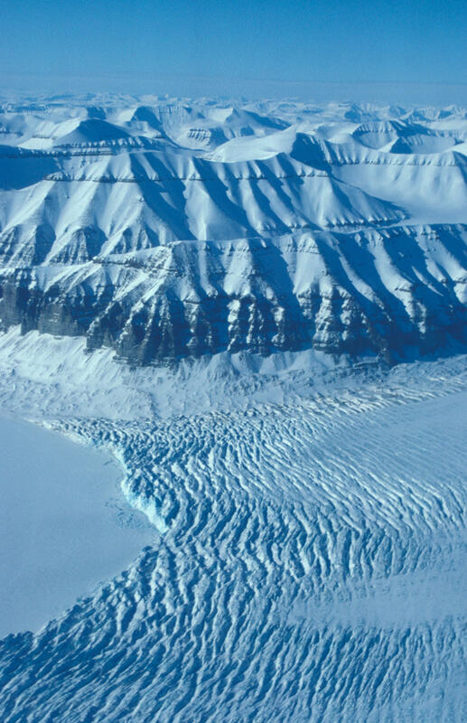 Bilde av isbre, med frosset havis. Snødekt fjellkjede i bakgrunnen.