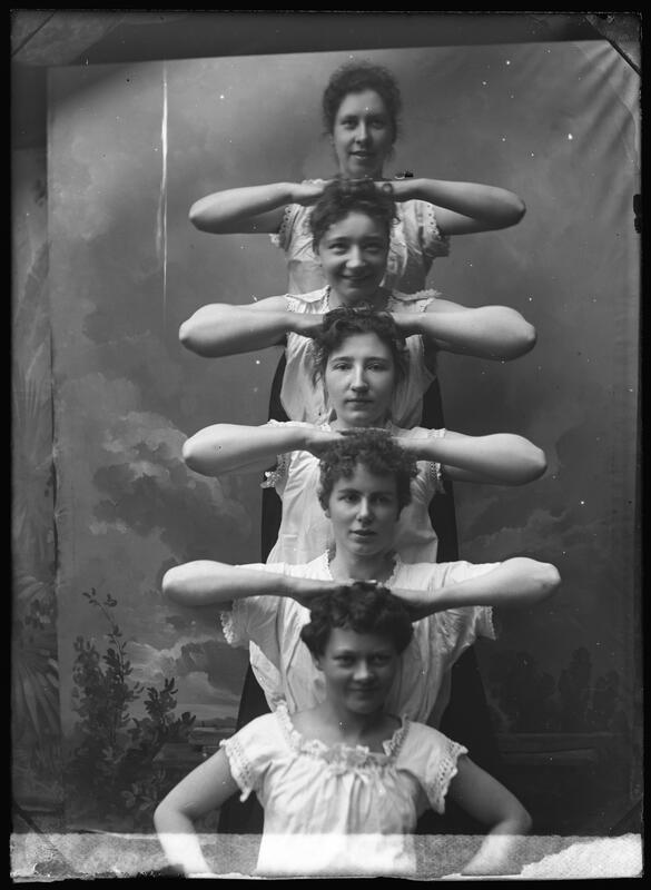 Fem kvinner i en menneskelig pyramide, stablet oppå hverandre med albuene ut slik at de lager et slags mønster