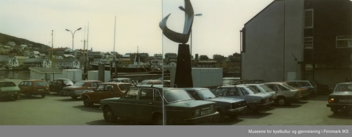 Honningsvåg, Holmen. Parkering på torget i sentrum. T.h. Kreditkassen-Fiskernes Bank. I midten skulpturen "Boreas". Sommeren 1985.