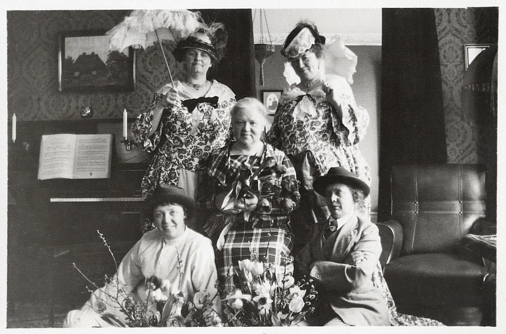 Födelsedagsuppvaktning av en äldre kvinna, med några utklädda damer i diverse kostymer.