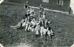 Flere ungdommer og barn sitter i en gresskledd bakke nedenfo