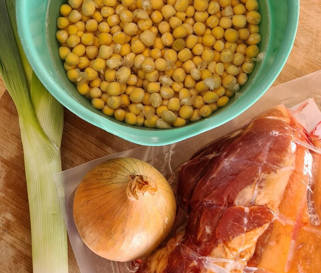 Bildet viser ingredienser til ertersuppe. Erter i en bolle, gressløk, løk og kjøtt