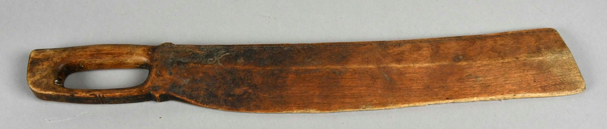 Skakekniv av ett trestykke med håndtak og knivblad. Utskåret bård øverst på knivbladet, både på siden og på kanten.
