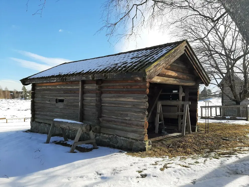 Bildet viser en eldre lintørke. Huset er laftet. Det er snø på bakken.