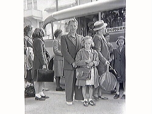 Reslädda flickor med sina förälrar står framför en buss på Öland, skyltad "Borgholm". Fotografen var där i samband med SLU:s riksting. Flickan som står med sin far (sannolikt) är okänd, men fick vara med som "statist" i bilden. Hon är klädd i basker, kappa och klänning med korta sockar i skorna med rosetter och bär en axelremsväska.