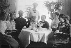 Gruppebilde av syv kvinner og to menn rundt et bord med kaff