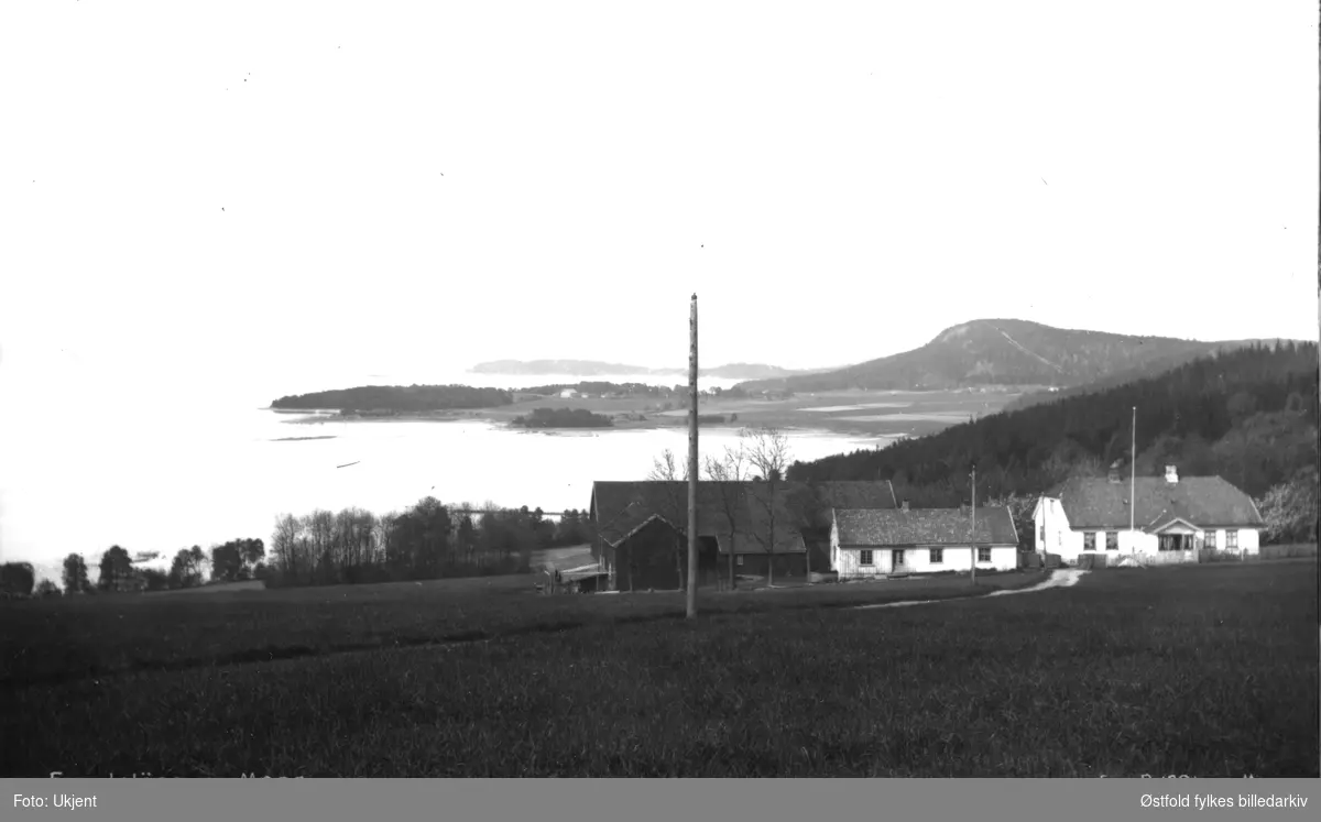 Utsikt fra øvre Ramberg mot nord med Bjørneåsen til høyre i bakgrunnen, Jeløy, MOss. Gården på sletta i bakgrunnen er Brevig gård. Oslofjorden til venstre. Postkort ca. 1920.