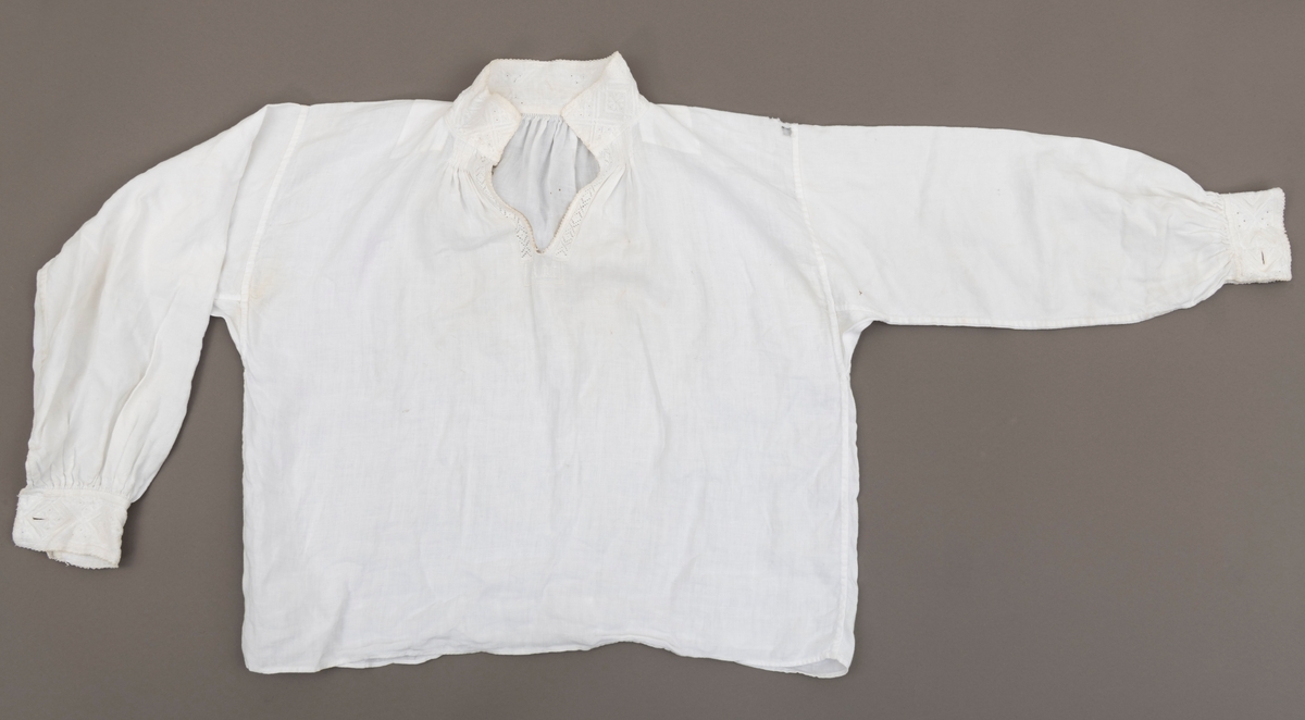 Bunadsskjorte med rik broderidekor i halslinning og ermlinning. Skade (slitasjehull) på venstre skulder.