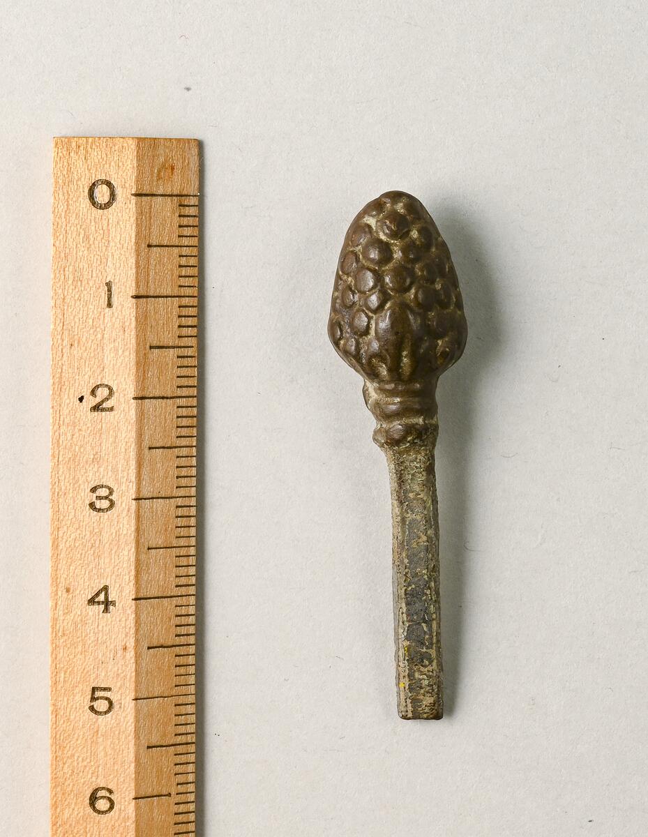 Liten nål av brons  till dräktspänne med hål i ena änden, något tillböjd.
av Brons, längd 52 mm.