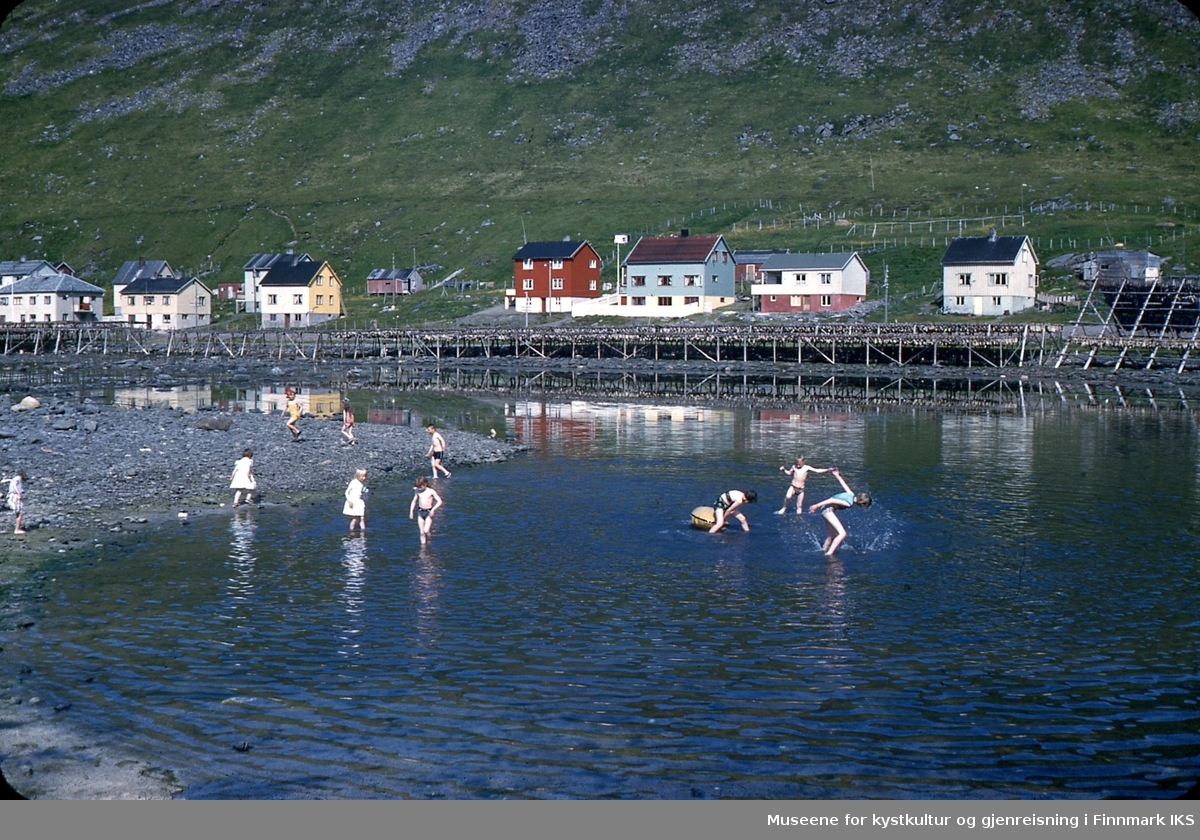Skarsvåg. Barn bader i sjøen. I bakgrunnen deler av bebyggelsen og mange fiskehjeller.