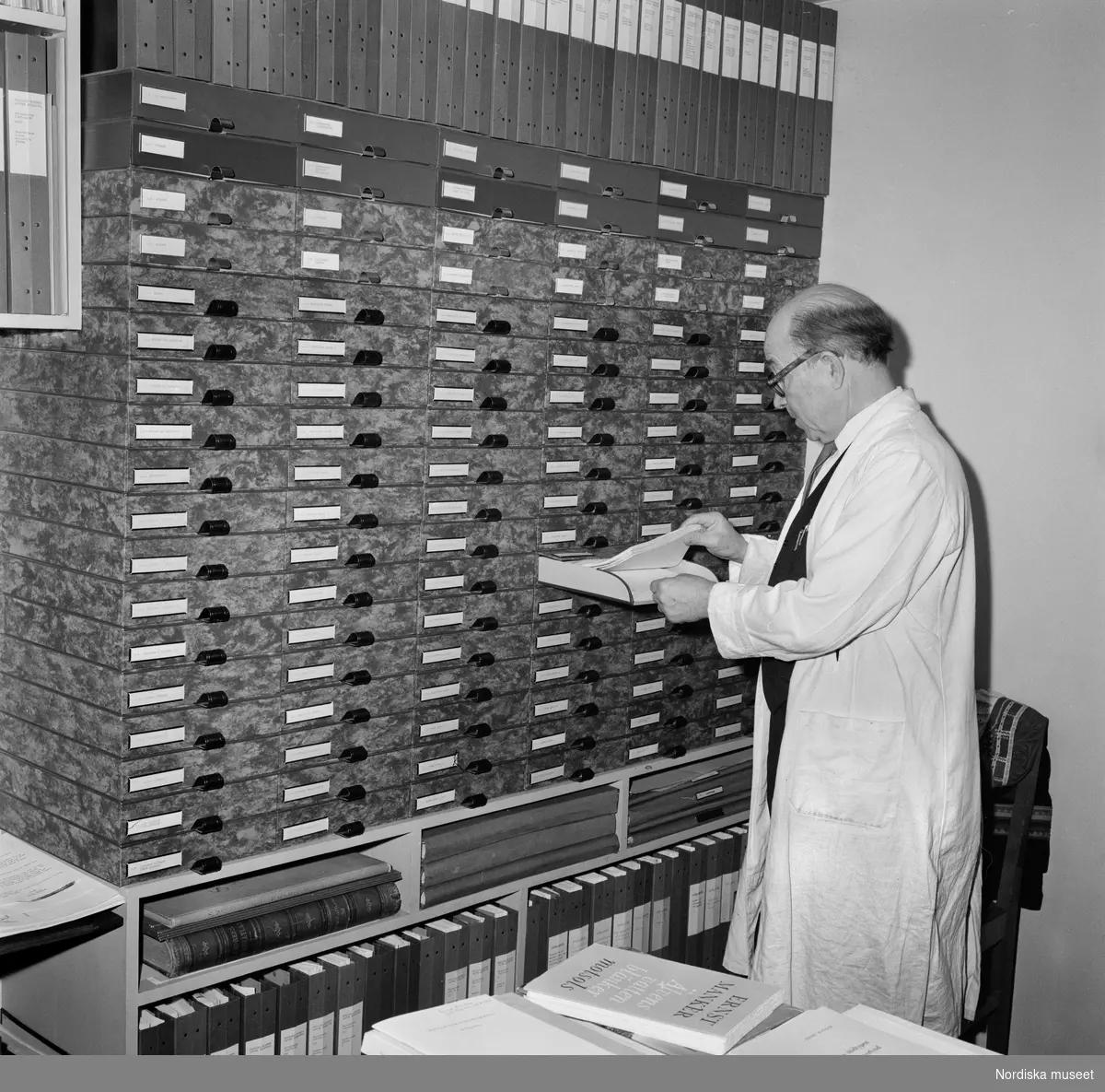 Ernst Manker vid en del av det så kallade Lapska arkivet. Han är klädd i vit arbetsrock och drar ut en av lådorna i hyllsystemet.