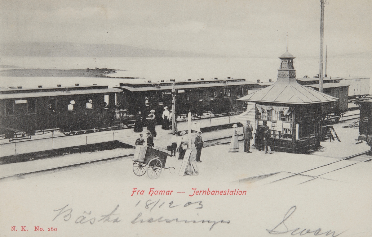 Postkort, Hamar jernbanestasjon, Narvesen kiosk fra 1894, tog med jernbanevogner, reisende på perrongen, 2 utgivelser med samme motiv, den ene er sterkt retusjert,