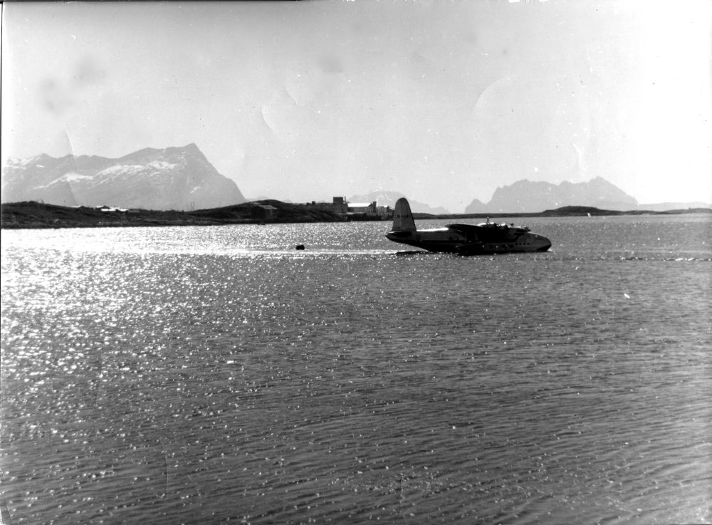 En Short S.25 Sandringham fra DNL taxer ut fra Bodø før avagang. I bakgrunnen Langstranda (Bodø) og fjellene Sandhornet og Fugløya (Gildeskål)