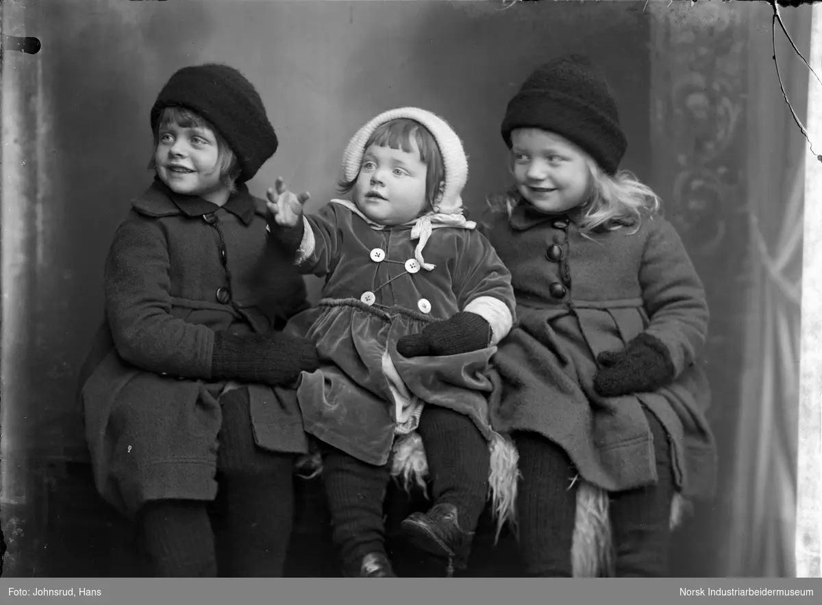 Portrett. Tre barn i yttertøy sittende i fotostudio.