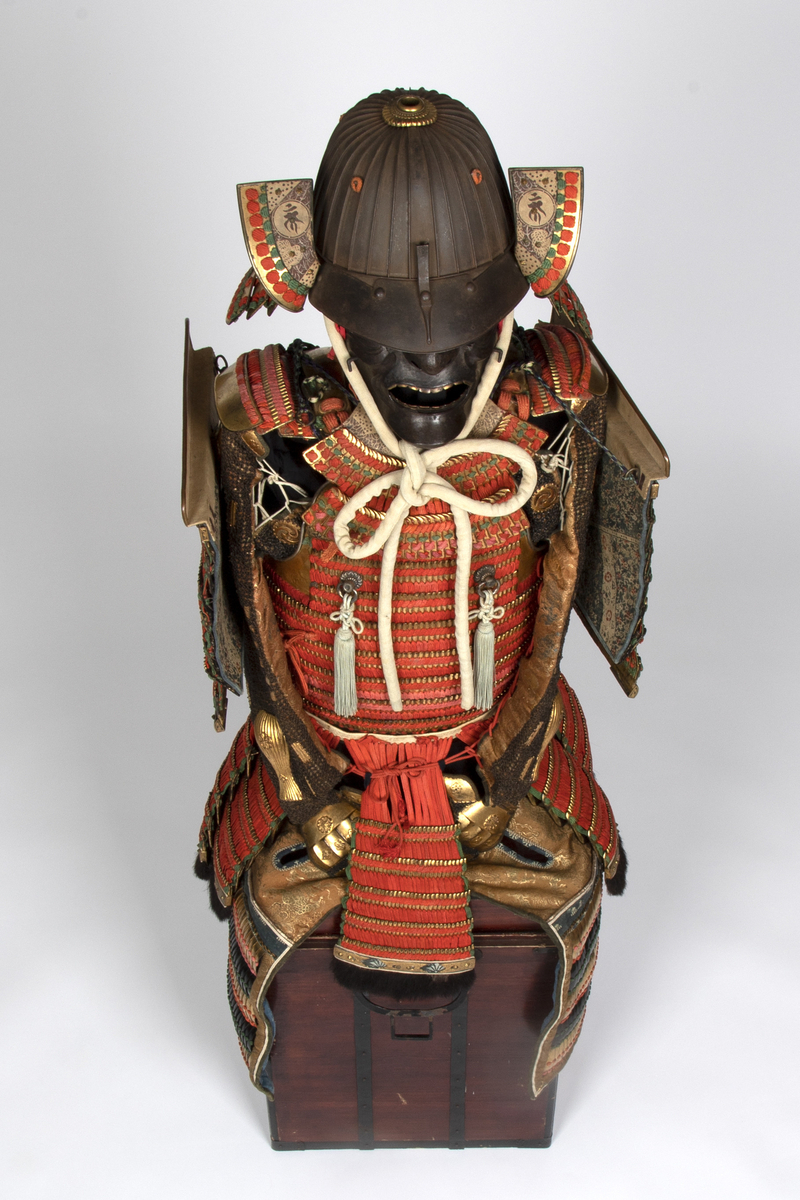 Drakten består av livstykke med skjørtepaneler, brynje, krage, ermslag (plater), hjelm, maske, beskyttere som dekker lår og legger (sistnevnte ikke avbildet på hovedbildet) og to løse armbeskyttere. Mange av delene er knyttet sammen med røde, flate silkesnorer. Hjelmen er en 32 Ken Suji Kabuto m/forgyldt Shikoro (nakkebeskyttelse). Tallet 32 betyr at hjelmen er konstruert av 32 rillede plater. Mempo (masken) har avtagbar nesebeskyttelse, svartlakkert innside og forgyldte tenner. Kabuto (hjelmen) med shikoro fungerer som beskyttelse, mens masken ble tatt i bruk for at samuraien skulle ha et mer skremmende utseende.