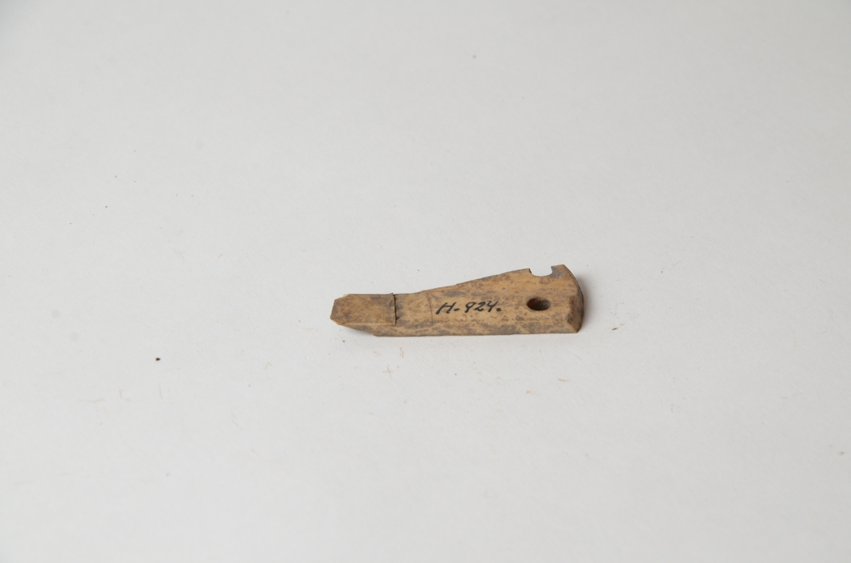 Ett föremål i ben med en ränna och två hål och på baksidan försedd med parallella räfflor. Föremålet har suttit i ett armborst.