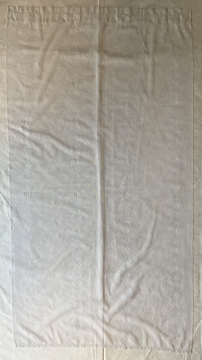 Avlang gardin i hvit nylon. Den har to vertikale border med blomster.