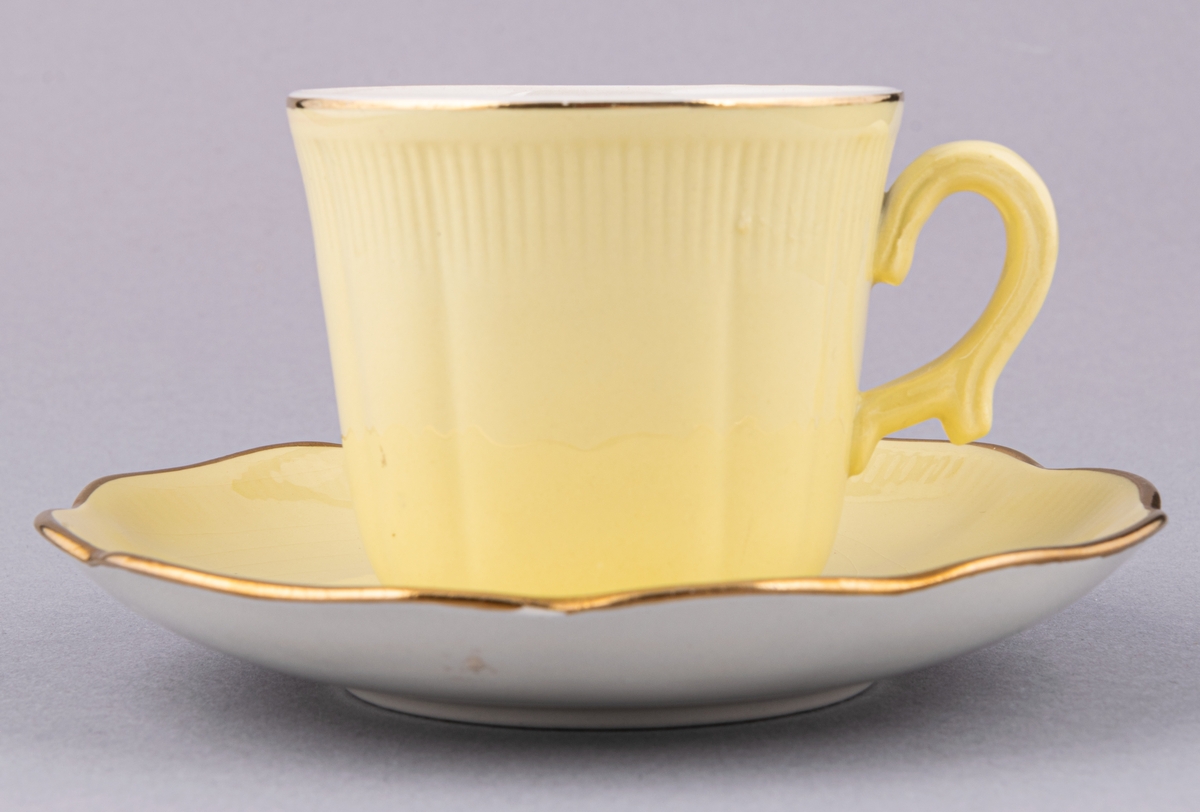 Kaffekopp med fat, flintgods. Modell AO, dekor Capri. Ljusgul glasyr på ovansidan, vit innuti, smal guldrand. Tillverkad vid Gefle Porslinsfabrik omkring 1949.