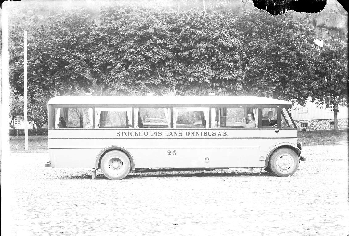 En buss parkerad på övre (östra) delen av Gränna torg. Två män tittar ut genom dess fönster. Bussen är märkt: "Stockholms Läns Omnibus AB 26"