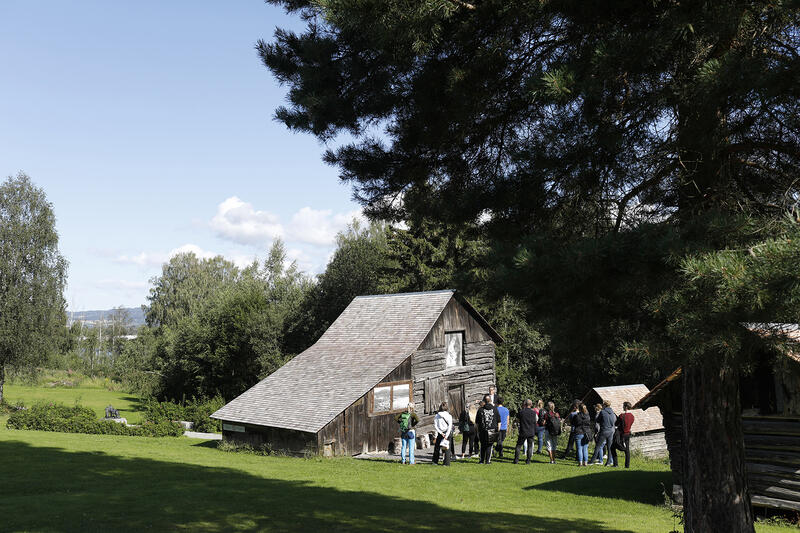 En gruppe mennesker står foran en av bygningene på friluftsmuseet under en omvisning av friluftsmuseet.