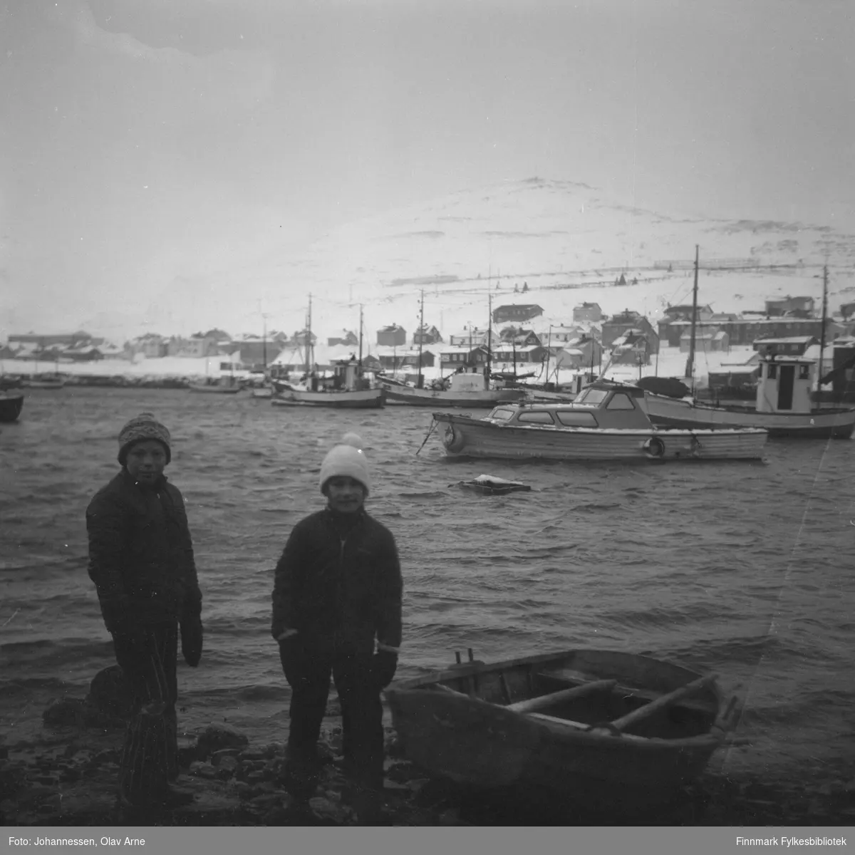 To ukjente gutter står ved siden av er robåt i Båtsfjord, Finnmark 

Foto trolig tatt på tidlig 1970-tallet