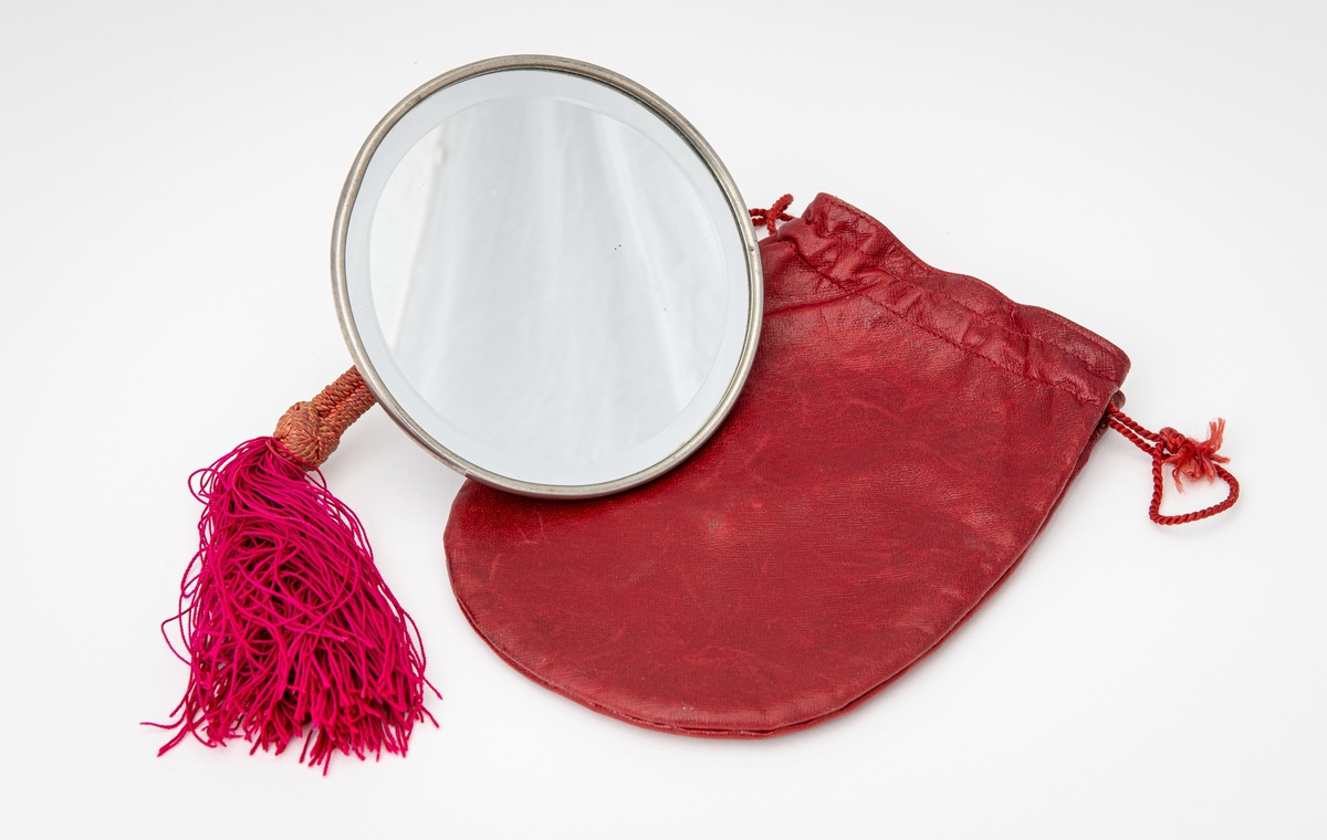 Rundt speil oppbevart i en rød skinnlomme med sammentrekkbar munning.
