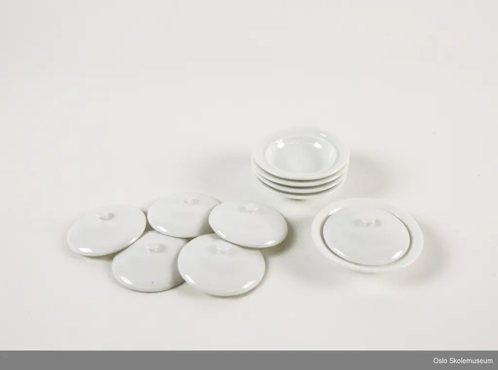 Fem hvite porselensfat i miniformat med seks tilhørende lokk. Hvert fat er merket med stempel fra Porsgrunds Porselensfabrikk på undersiden.