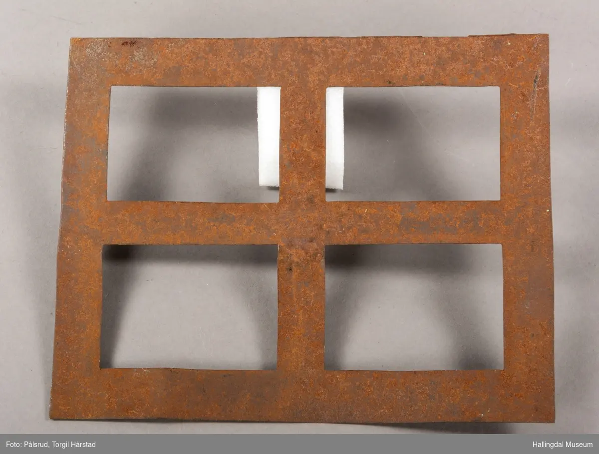 En rektangulær mal i rustet jern, med fire mindre rektangulære åpninger - formet som et vindu.