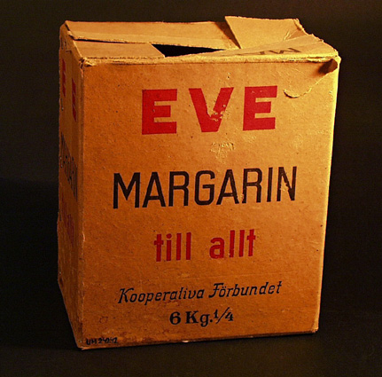Kartong av oblekt papp med svart och rött tryck: EVE MARGARIN till allt, Kooperativa förbundet 6kg 1/4. Remsor av förpackningstejp kvar.