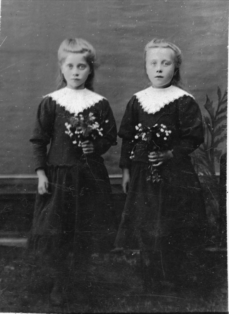 Studioportrett av tvillingsøstre med blomsterbuketter.