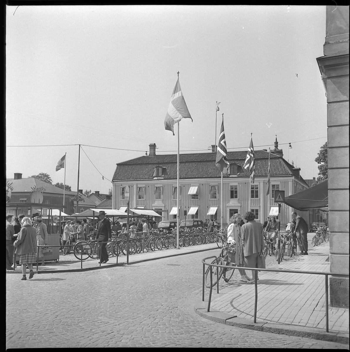 Norska och svenska flaggor hissade vid Stora torget och Rådhuset, 4 juni 1950. Kiosk med försäljning av Tyrol-glass ligger i hörnet av torget.