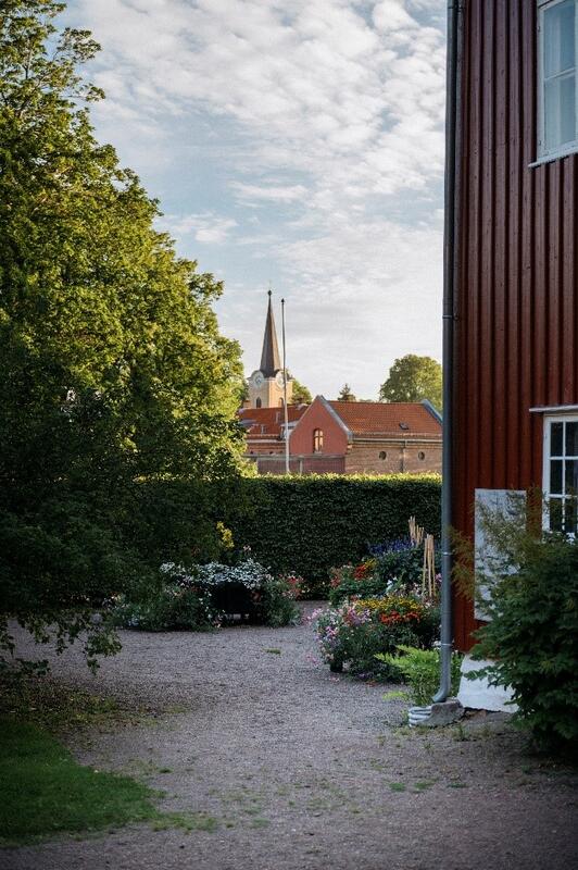 I en hage i Herregården i Larvik. Helt i horisonten skimtes et kirketårn. Det er sommer og grønne busker rundt