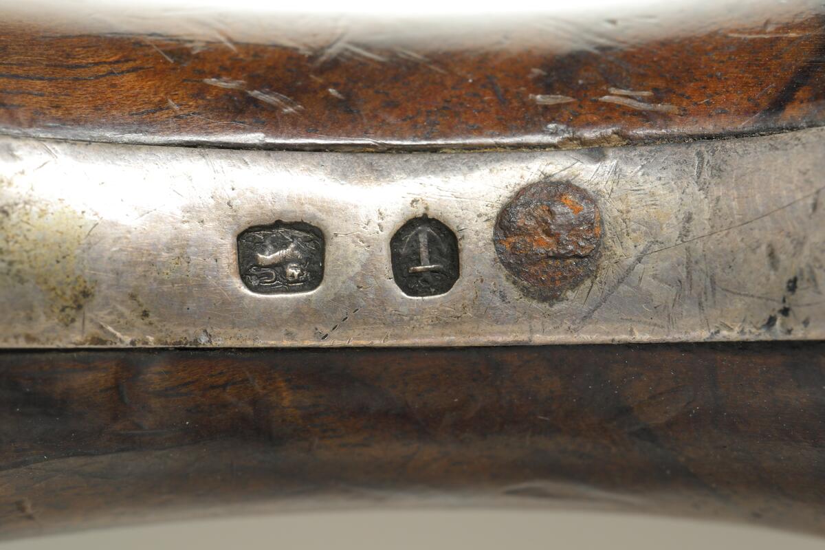 Flintlåspistol med helstock och lås i stål i s.k. Centuckystil. Pipan är gjord i mässing, och kolvkappa, varbygel, sidobleck, tumplåt och rörkor i silver. Pipan är märkt "ST-966", samt två kontrollstämplar från London, och som är åttakantig i formen, men övergår i cylindrisk form ut mot mynningen. Kolvkappan har silverstämplar från Birmingham, varbygeln likaså. Sidoblecket är utformat som blomsterslingor, och kolvkappan som en maskaron. Varbygeln är ornamenterad med en blomma i en oval. Längst fram är den utformad som ett ekollon. Tumplåten är märkt med "EC". Laddstock finns under framstocken.
Inskrivet i huvudkatalogen 1974.