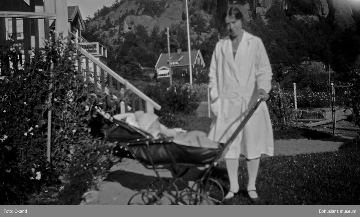 En person med en baby i en barnvagn i en trädgård.