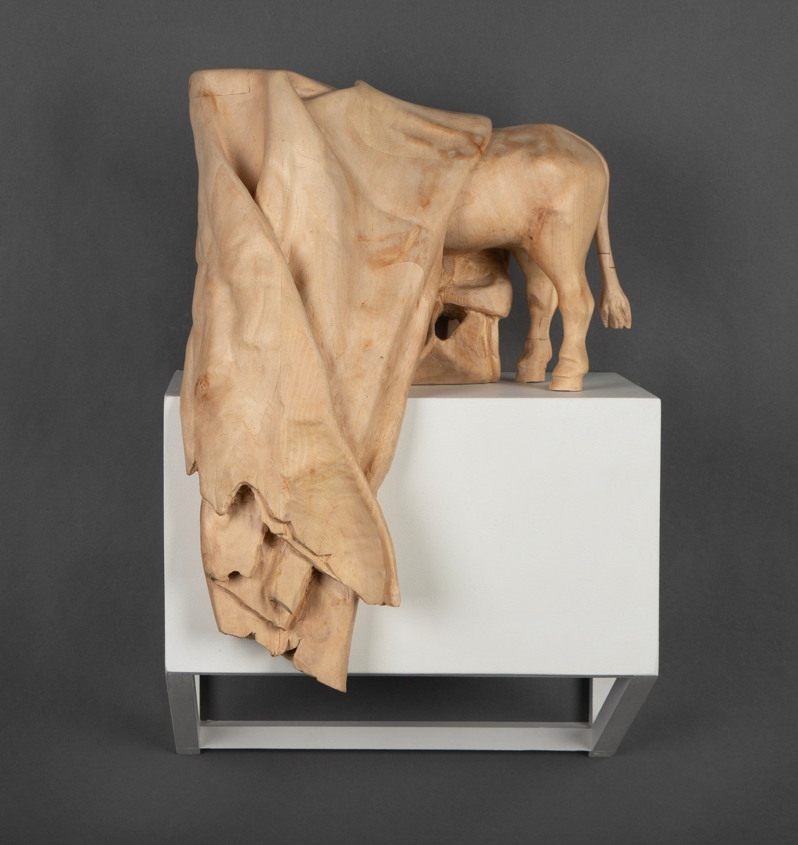 Treskulptur av en ku foldet inn i et tøystykke.