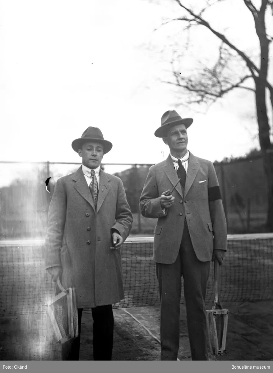 Två personer hållandes tennisracket framför ett tennisnät.