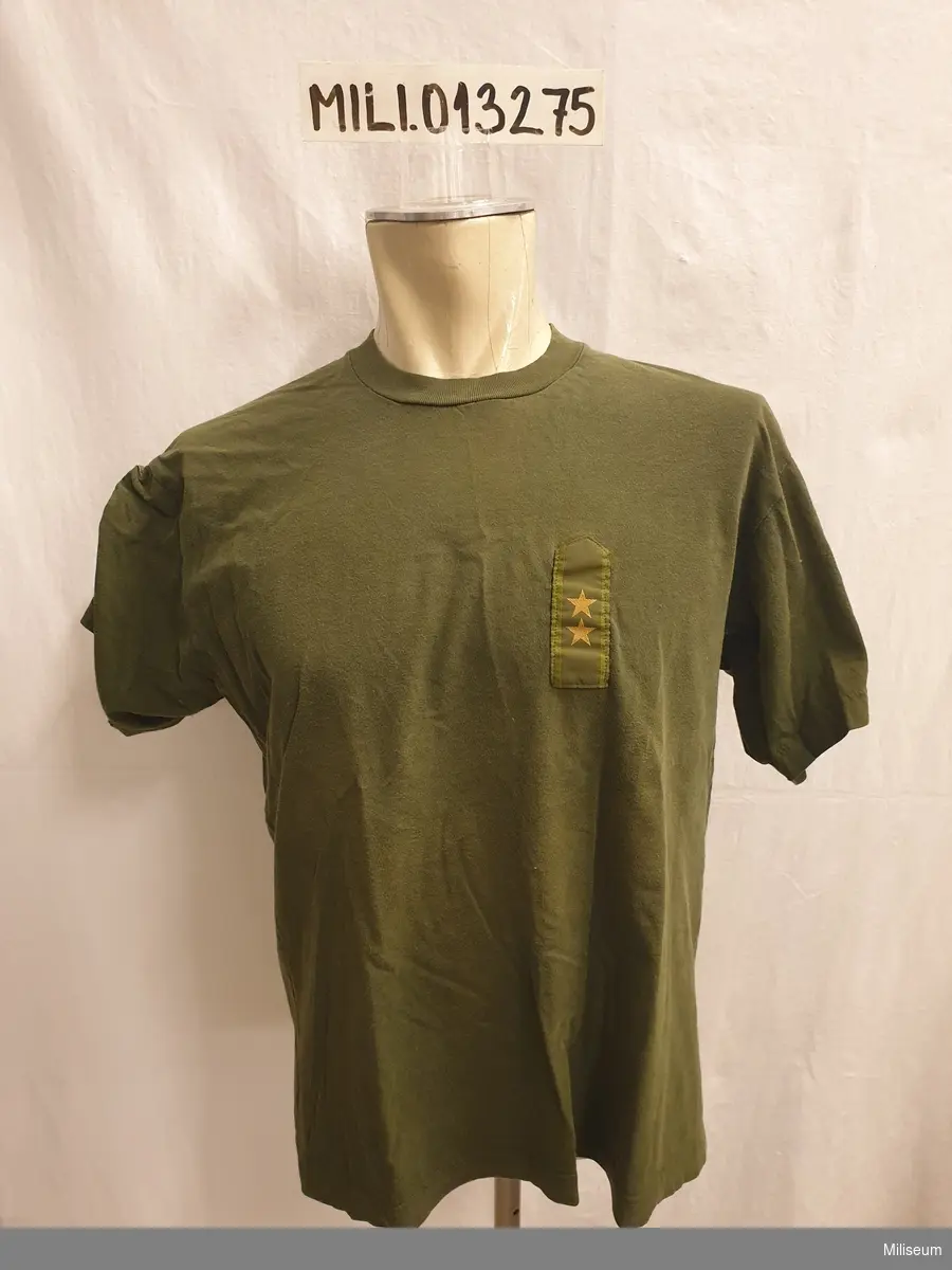 T-shirt 90, grön, storlek 5. Försedd med gradbeteckning för löjtnant och nationalitetsmärke för utlandstjänst. Tillverkad i Indien.