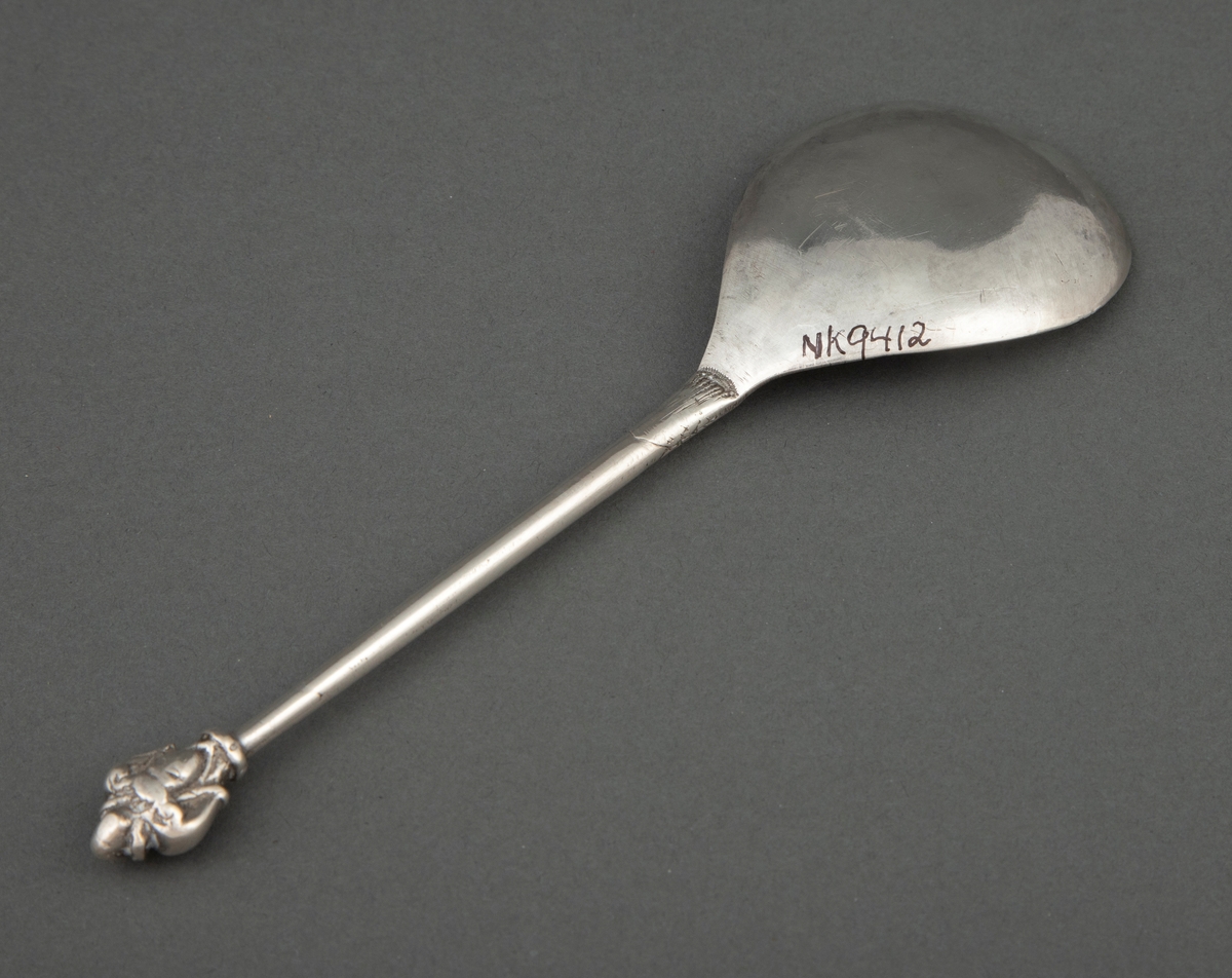 Kjerubskje i sølv med dråpeformet skjeblad og ornamentert skaft. Skaftenden er dekorert med kjerubhoder på for- og baksiden.