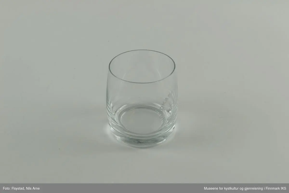 Et rundt brennevinsglass, eller cocktailglass uten stett og trykt tekst på siden av glasset. 

Glasset har en tykk bunn med tynne sider. Øverst står  "NORDKAPPTUNNELEN"  og nederst står "VEIDEKKE". Ordene danner en sirkel og "Gjennomslag 13.5.1998" er trykt inne i sirkelen. Helt nederst står "DYNO".   