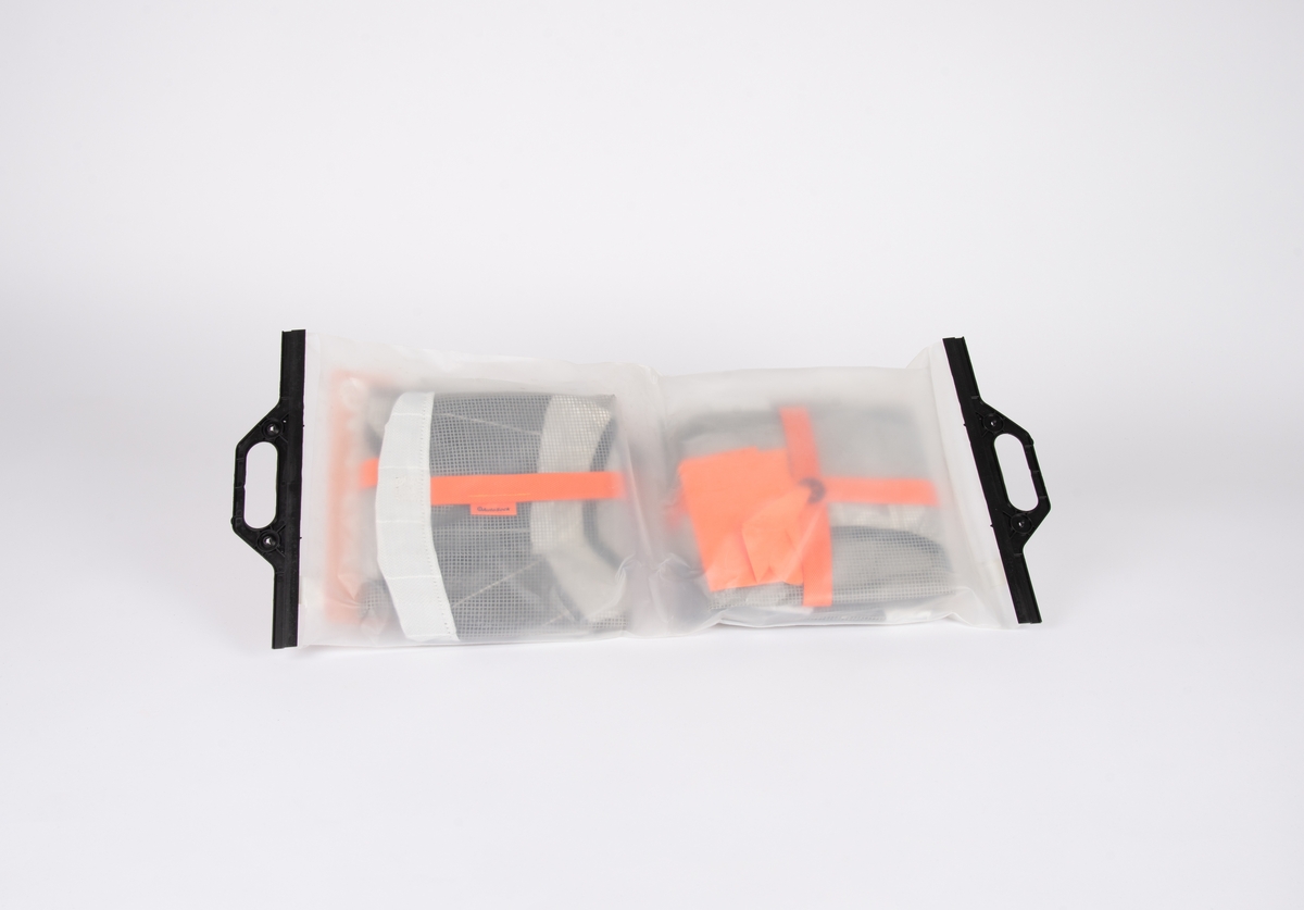 Sirkulær hjulsokk i syntetisk tekstil kantet med elstikk til feste rundt hjul.

Et par oransje plasthansker med sveisede sømmer.

Plastpose med sort håndtak som lukker posen.