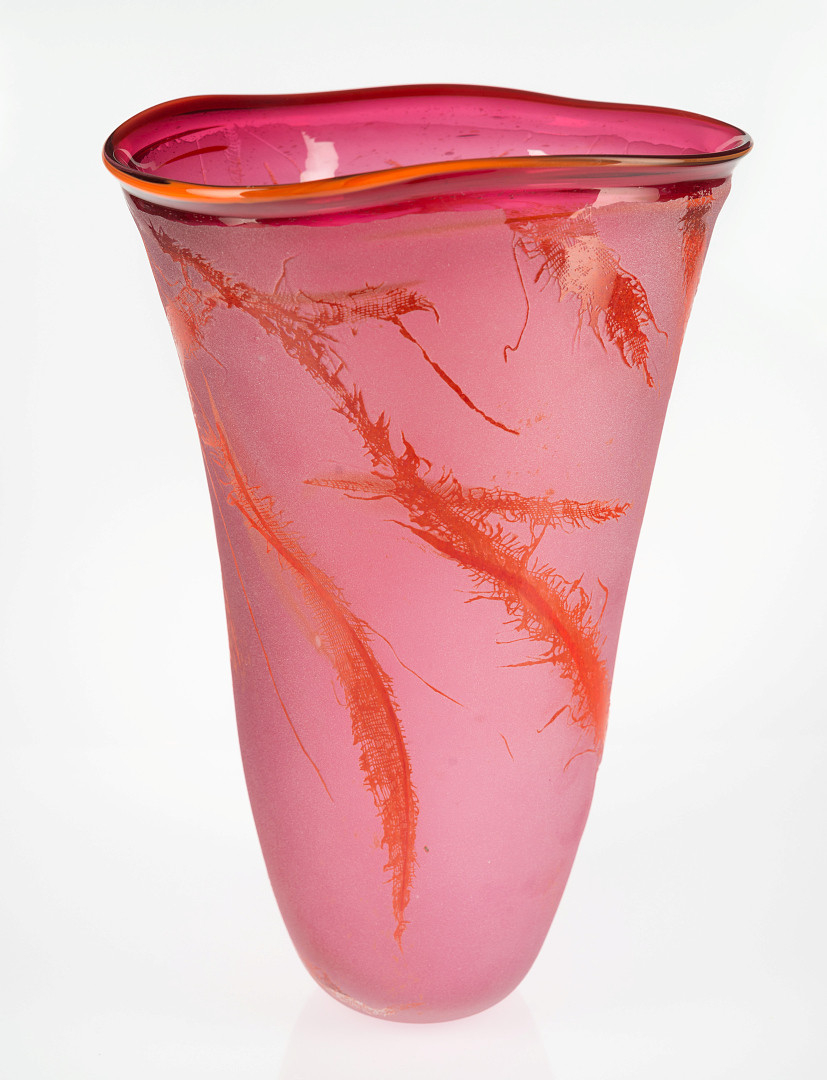 Konisk vase i halvgjennomskinnelig rosafarget glass. Ujevn formet munningrand i oransje. Overflaten er mattet og dekorert med fjærlignede former i rødt.