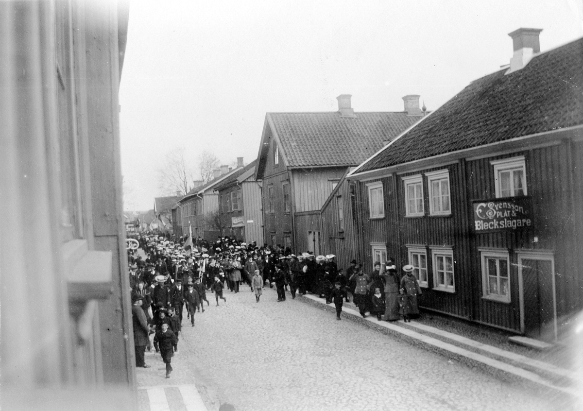 Första majtåg i kvarter Friden, Drottninggatan mellan Färgaregatan och Torggatan. Fastigheten riven 1910.